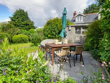 An outdoor patio with a wooden table and six chairs surrounded by greenery and flowers at 1 Cheriton Row Carew Cheriton Nr Tenby Pembrokeshire