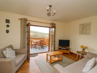 A living room with two sofas a coffee table a TV on a stand and an open door leading to a balcony with a table and chairs at Llaethdy in Cardigan