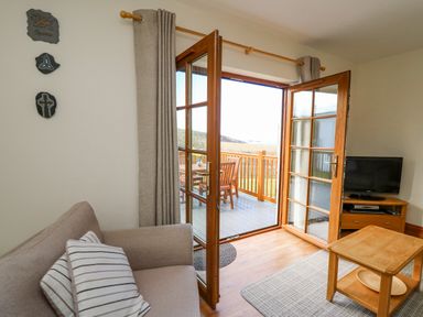 A living room with a sofa a coffee table and a television near open double doors leading to a deck with wooden furniture at Llaethdy in Cardigan