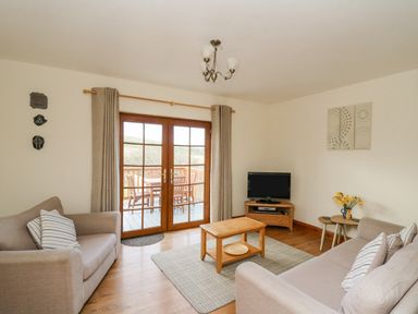 A living room with two sofas a wooden coffee table television and glass doors leading to a balcony at Llaethdy in Cardigan