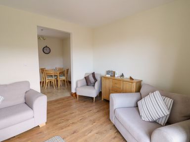 A sitting room with two sofas, an armchair, wooden cabinet and a dining area visible through an opening at Llaethdy in Cardigan