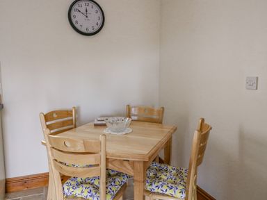 A dining area with a wooden table and four chairs with floral cushions and a wall clock at Llaethdy Cardigan