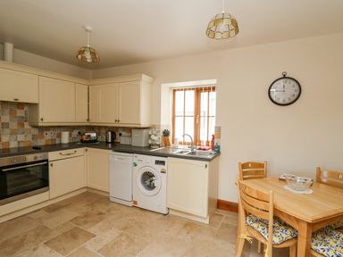 A kitchen with cream cabinets a washing machine dishwasher oven and a wooden dining table with chairs at Llaethdy in Cardigan