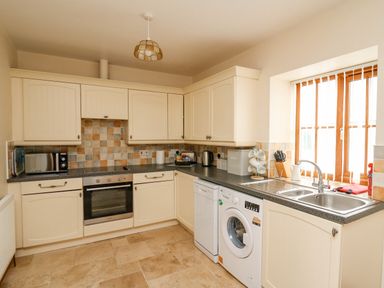 A kitchen with cream cabinets and tiled backsplash with oven dishwasher washing machine and microwave at Llaethdy in Cardigan