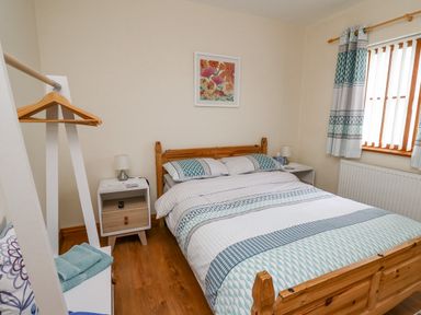 A bedroom with a wooden bed a bedside table with a lamp and a shelving unit with hangers and towels at Llaethdy in Cardigan