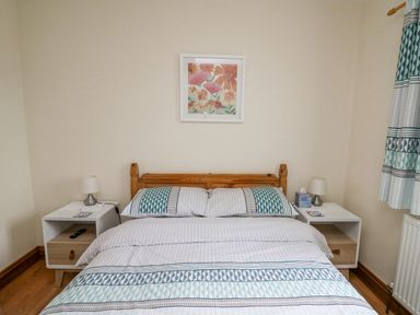 A bedroom with a bed between two nightstands each with a lamp and a framed floral picture on the wall at Llaethdy in Cardigan