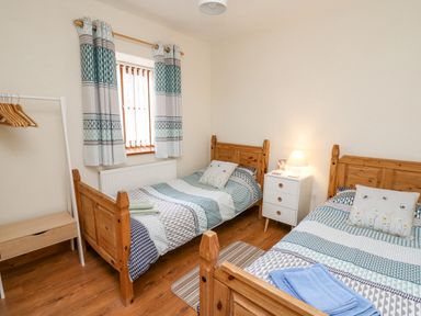 A bedroom with two wooden single beds a white bedside table with lamp a window with curtains and a clothes rack at Llaethdy in Cardigan