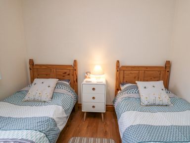 A bedroom with two single beds and a white nightstand with a lamp between them at Llaethdy in Cardigan