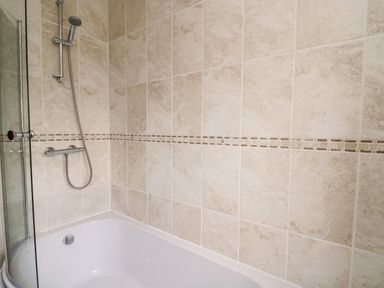 A bathroom with a bathtub shower and beige tiled walls at Llaethdy in Cardigan