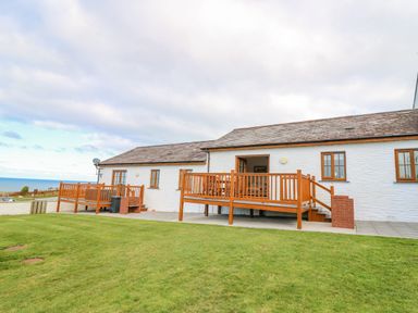 An outdoor view of a white house with two wooden decks and a grassy lawn at Llaethdy in Cardigan
