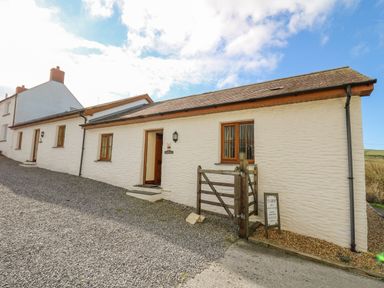 A white exterior building with wooden windows a wooden gate and a gravel driveway at Beudy in Mwnt Cardigan Ceredigion