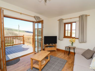 A living room with a sofa a coffee table a tv on a stand and an open door leading to a balcony at Beudy in Mwnt Cardigan Ceredigion