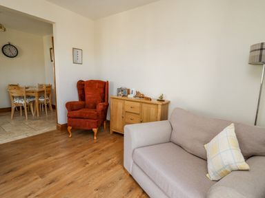A living room with a red armchair beige sofa wooden sideboard and a floor lamp at Beudy in Mwnt Cardigan Ceredigion