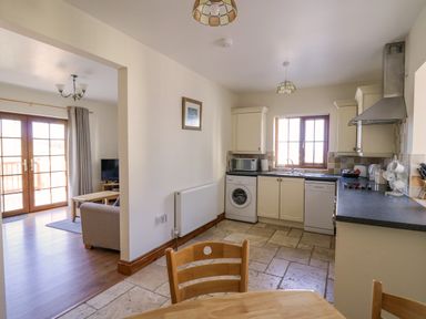 A kitchen with a washing machine dishwasher microwave and dining table next to a living room with sofa and television at Beudy in Mwnt Cardigan Ceredigion