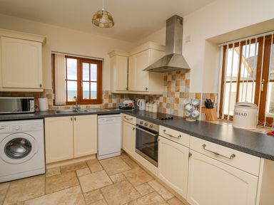 A kitchen with cream cabinets washing machine dishwasher oven and windows at Beudy in Mwnt Cardigan Ceredigion