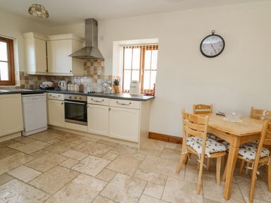 A kitchen with white cabinets a stove dishwasher table and chairs with cushions at Beudy in Mwnt Cardigan Ceredigion