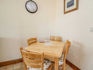 A wooden dining table with four chairs and a clock on the wall at Beudy in Mwnt Cardigan Ceredigion