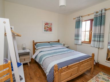 A bedroom with a wooden bed and side tables and a window with patterned curtains at Beudy in Mwnt Cardigan Ceredigion