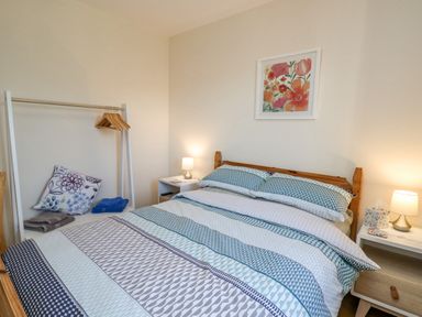 A bedroom with a double bed with patterned bedding two bedside tables with lamps and a white clothing rack with hangers and folded towels at Beudy in Mwnt Cardigan Ceredigion