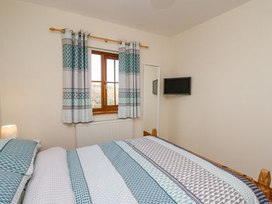 A bedroom with a bed a window with curtains a wall-mounted television and a full-length mirror at Beudy in Mwnt Cardigan Ceredigion