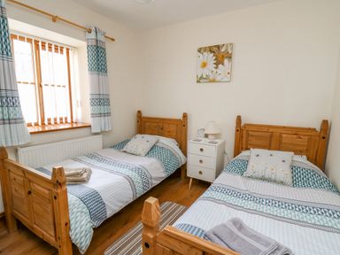 A bedroom with two single wooden beds white bedside table and window with curtains at Beudy in Mwnt Cardigan Ceredigion