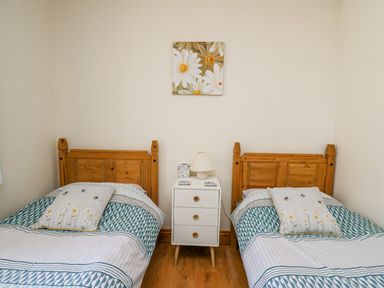 A bedroom with two single wooden beds separated by a white nightstand with a lamp and daisies wall art at Beudy in Mwnt Cardigan Ceredigion