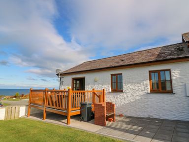 A white cottage with wooden windows and a raised wooden deck overlooking the sea at Beudy in Mwnt Cardigan Ceredigion