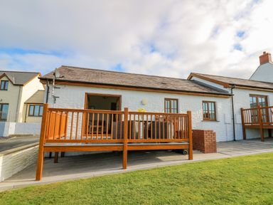 Exterior view of a white building with a brown wooden deck and green lawn at Beudy in Mwnt Cardigan Ceredigion