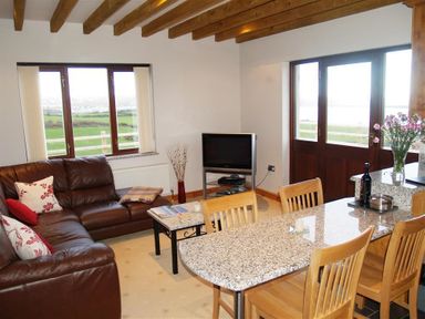 A living room with a brown leather sofa a small coffee table a television and a dining table with wooden chairs at Cable Cottage in Fishguard Pembrokeshire