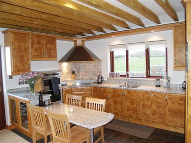 A kitchen with wooden cabinets a granite countertop wooden beams on the ceiling and a window with a view at Cable Cottage in Fishguard Pembrokeshire
