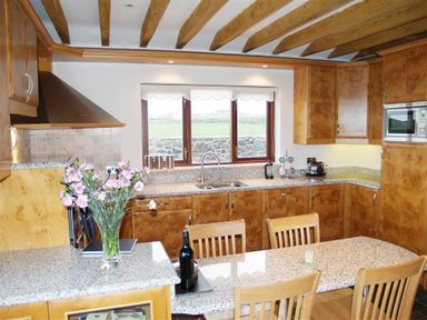 A kitchen with wooden beams wooden cabinets and granite countertops at Cable Cottage in Fishguard Pembrokeshire