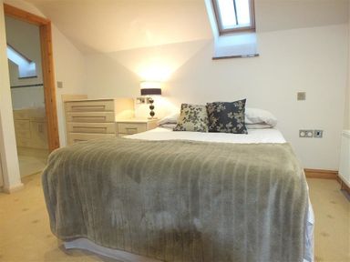 A bedroom with a bed a dresser a lamp and a skylight window at Cable Cottage in Fishguard Pembrokeshire