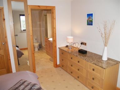 A bedroom with a wooden dresser a lamp and a vase with decorative branches next to a door leading to a bathroom at Cable Cottage in Fishguard Pembrokeshire