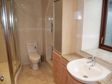 A bathroom with a toilet a shower a sink with granite countertop and wooden cabinets at Cable Cottage in Fishguard Pembrokeshire
