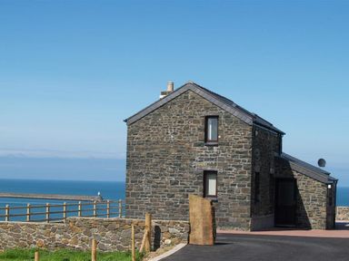 A stone house with two windows and a door near a stone wall overlooking the sea at Cable Cottage in Fishguard Pembrokeshire