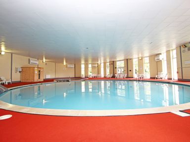 An indoor swimming pool with red flooring and white chairs around at 9 Manorcombe Bungalows St Ann's Chapel near Callington