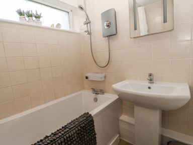 A bathroom with a bathtub a sink a wall-mounted shower unit and a window with small flower pots at 9 Manorcombe Bungalows St Ann's Chapel near Callington