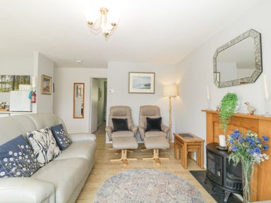 A living room with a sofa and armchairs next to a fireplace with flowers on the floor at 9 Manorcombe Bungalows St Ann's Chapel near Callington