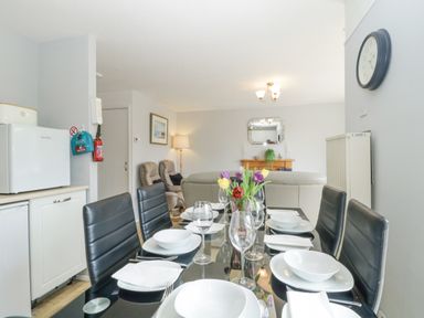 A dining table set with plates glasses and cutlery in an open plan living room with chairs a sofa a mirror and a clock at 9 Manorcombe Bungalows in St Ann's Chapel near Callington