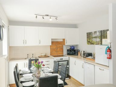 A kitchen with white cabinets a dining table set with plates and glasses and kitchen appliances at 9 Manorcombe Bungalows St Ann's Chapel near Callington