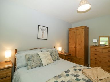 A bedroom with a bed and pillows two bedside tables with lamps a wooden wardrobe and dresser at 9 Manorcombe Bungalows in St Ann's Chapel near Callington