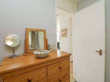 A wooden dresser with round knobs and a small mirror bowl and tissue box on top in a room with an open white door at 9 Manorcombe Bungalows in St Ann's Chapel near Callington