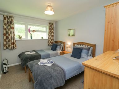 A bedroom with two single beds a nightstand with a lamp wooden wardrobe and a window with patterned curtains at 9 Manorcombe Bungalows St Ann's Chapel near Callington