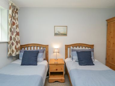 A bedroom with two single wooden beds a wooden nightstand with a lamp and a wooden wardrobe at 9 Manorcombe Bungalows St Ann's Chapel near Callington