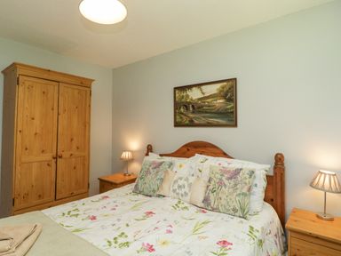 A bedroom with a wooden bed with floral bedding a wooden wardrobe and two bedside tables with lamps at 9 Manorcombe Bungalows St Ann's Chapel near Callington