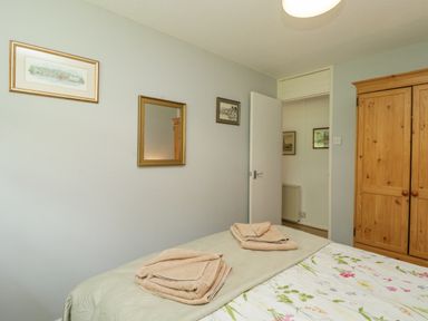 A bedroom with a bed with folded towels a wooden wardrobe and framed pictures on the wall at 9 Manorcombe Bungalows in St Ann's Chapel near Callington
