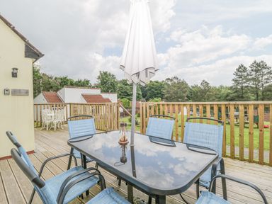 An outdoor wooden deck with a glass table and blue chairs under a closed white umbrella at 9 Manorcombe Bungalows St Ann's Chapel near Callington
