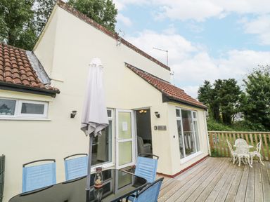 An outdoor wooden deck with a glass table and blue chairs and a white metal table with chairs at 9 Manorcombe Bungalows St Ann's Chapel near Callington