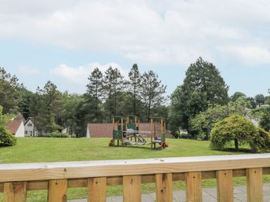 A playground with climbing equipment on grass surrounded by trees and houses at 9 Manorcombe Bungalows St Ann's Chapel near Callington