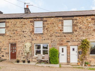 Stone terraced houses with doors and windows with potted plants and a bench outside at Peth Head Cottage in Wooler